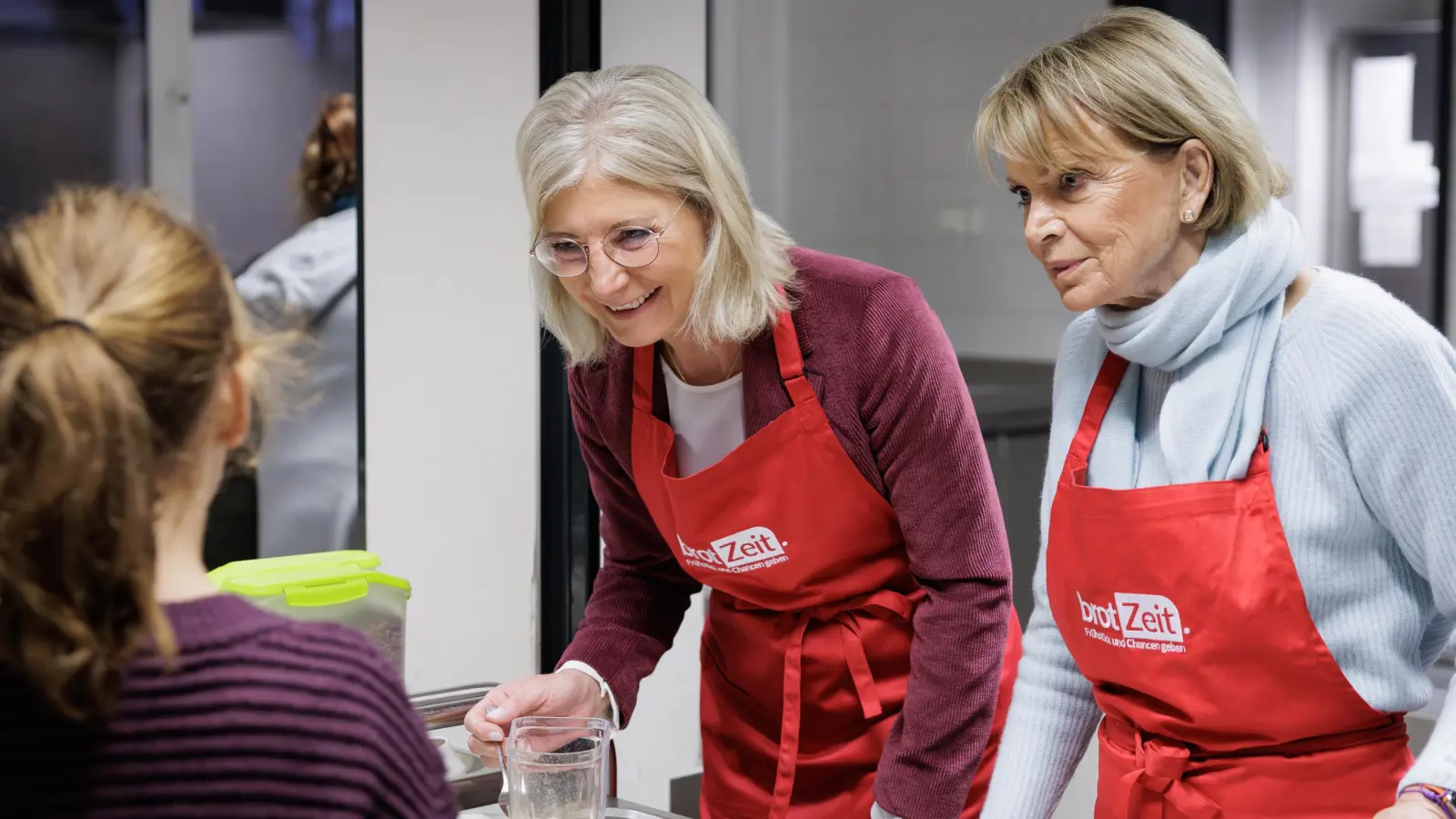 Bayerns Sozialministerin Ulrike Scharf (links) und die Vereinsgründerin und Aufsichtsratsvorsitzende von brotZeit, Uschi Glas, bei der Frühstücksausgabe an der Grundschule Weißenseestraße. (Foto: StMAS/Schäffler)