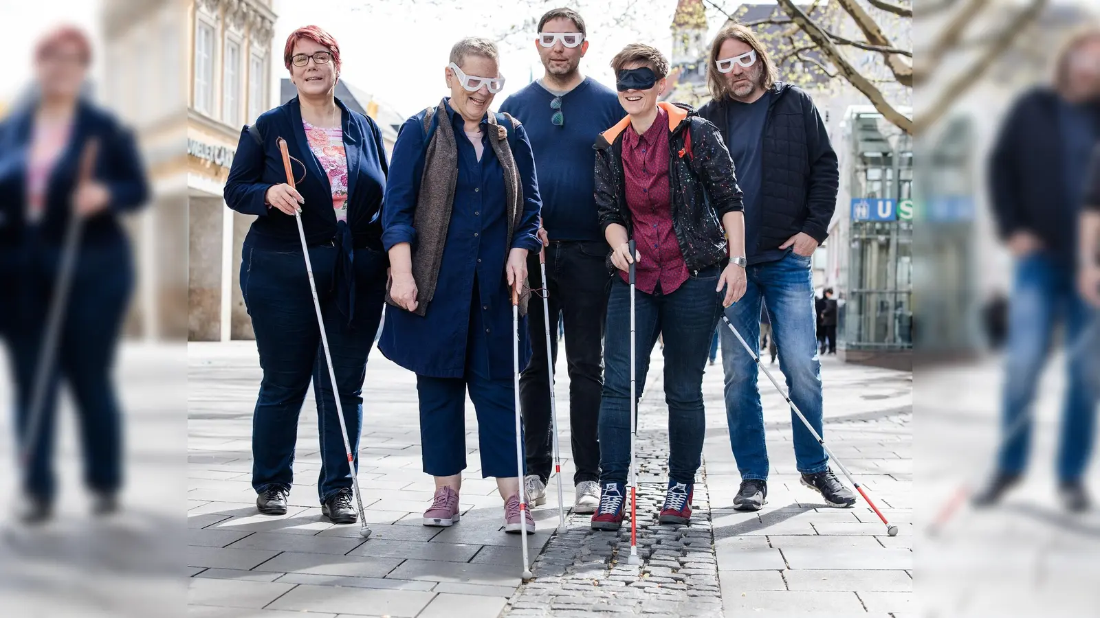 Stefanie Freitag (BBSB), Sofia Langmeier (Die Grünen), Stefan Jagl (Die Linke), Barbara Likus (SPD) und Roland Hefter (SPD) testen in der Fußgängerzone – ausgestattet mit Langstöcken und Simulationsbrillen – den sogenannten Leitstreifen, eine Regenrinne aus aus Pflastersteinen. (F.: Kerstin Keysers)