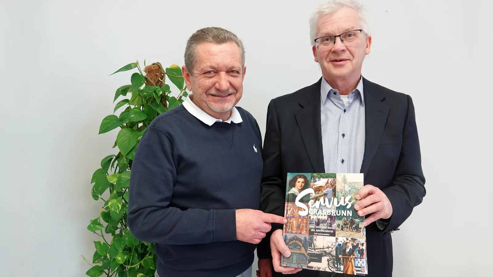 Grasbrunns Erster Bürgermeister Klaus Korneder (links) und Rolf Katzendobler, Ortschronist der Gemeinde Grasbrunn und Kreisdenkmalpfleger im Landkreis München, mit dem neu erschienenen Buch „Servus Grasbrunn. Eine Zeitreise durch die Jahrhunderte“. (Foto: Gemeinde Grasbrunn)