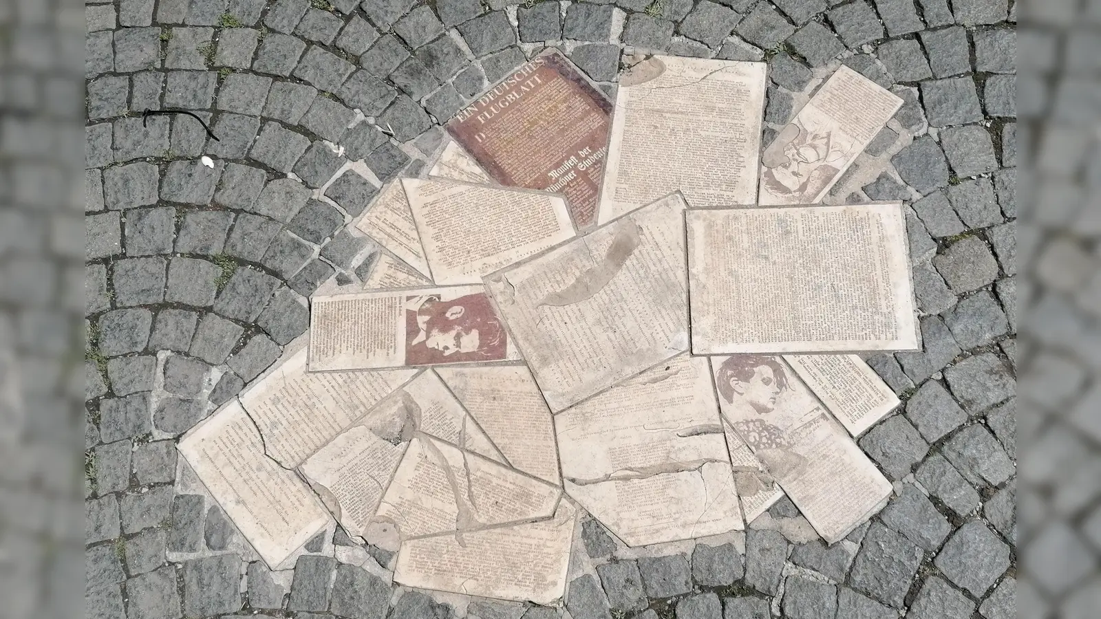 Ein Bodendenkmal des Künstlers Robert Schmidt-Matt vor dem Haupteingang der Universität zeigt seit 1988 Flugblätter, Portraitfotos und einen Abschiedsbrief von Willi Graf. Es setzt sich vom Haupteingang aus über den Geschwister-Scholl-Platz fort. (Foto: job)