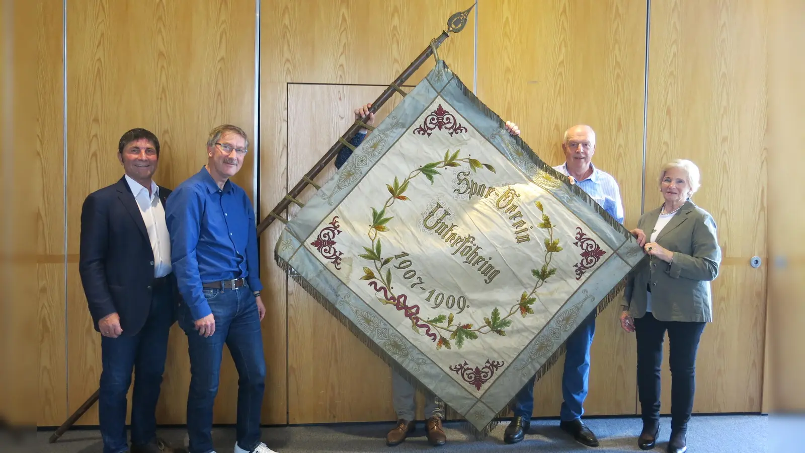 Von links: Bürgermeister Andreas Kemmelmeyer, Thomas Pöschl, Ortschronist Alois Riederer und Birgit Kullmann, Vorsitzende des Museums und Heimatvereins Feringer Sach, mit der 116 Jahre alten Fahne des Sparvereins. (Foto: Gemeinde Ufg/lih)